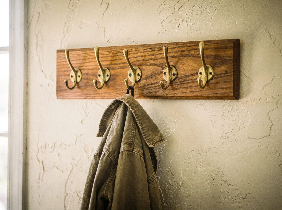 Solid oak wall-mounted coat rack with five brass hooks and a jacket hanging